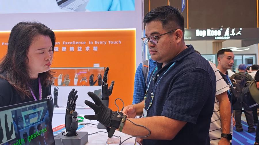 Daniel Chuquimango (D) opera uma mão biônica na seção de robôs de serviço da 138ª Feira de Cantão, em Guangzhou, na Província de Guangdong, sul da China, em 15 de outubro de 2025. (Foto de Wu Jiawei/Xinhua)