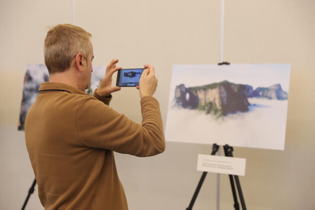 O locutor português da rádio Íris FM, Carlos Alves, tira fotos da montanha Tianmenshan, localizada em Zhangjiajie, na província chinesa de Hunan, durante a exposição fotográfica "Bem-vindos à Hunan", realizada em Lisboa, Portugal, em 23 de janeiro de 2026. (Xinhua/Xun Wei)